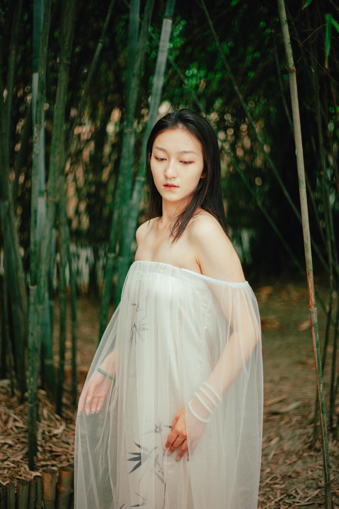 A woman in a delicate tulle dress stands gracefully amidst a serene bamboo forest.