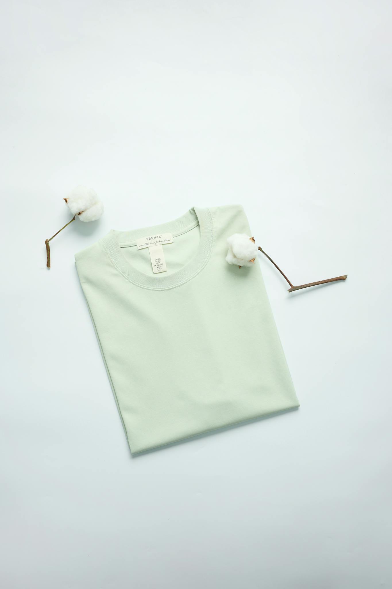 Minimalist photo of a folded mint green t-shirt with cotton stems for a natural fashion touch.